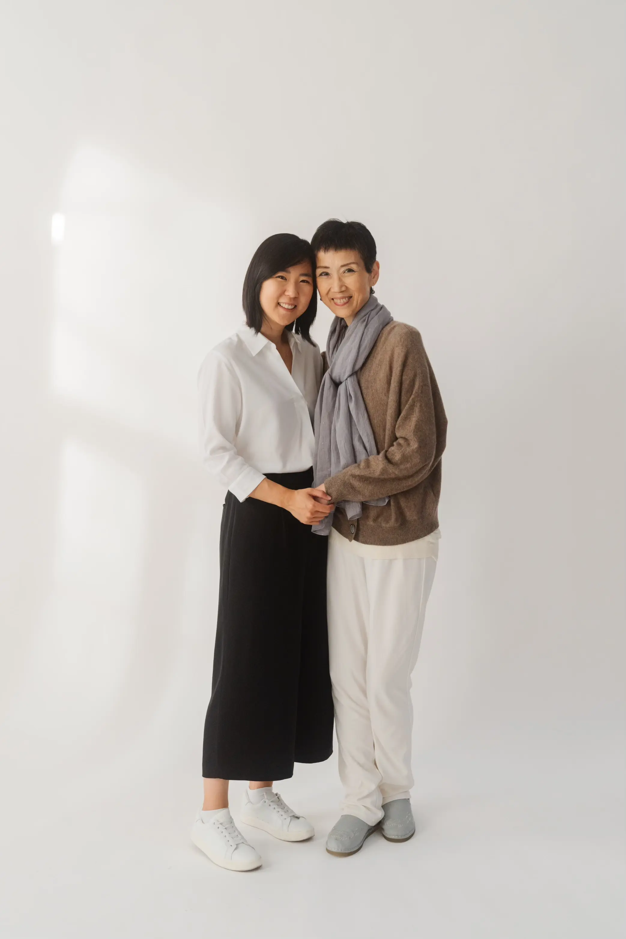 A photo of Kat (left) and her monther (right) both smiling into the camera on a simple background.